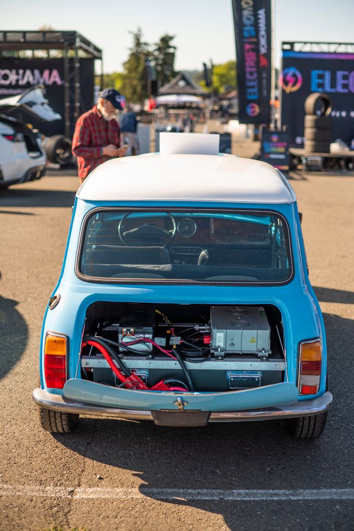 Rear view of a retro electric car with exposed battery compartment at a car show.