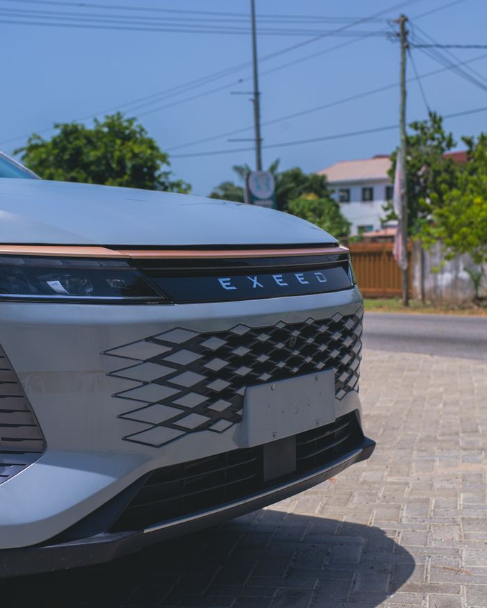 Side view of a sleek Exeed car under clear blue sky on a paved parking lot.